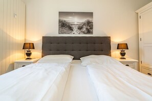 A double bed with white linens, two bedside lamps, a grey upholstered headboard, and a black and white landscape painting above the bed. - Stadtresidenz App. 4 - Ebenerdige, Moderne Stadtwohnung- Kurze Wege zum Strand, mit Eigener (Sylt)