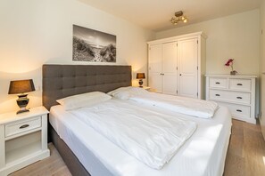 A bedroom with a large bed, two bedside tables with lamps, a wardrobe, and a framed picture on the wall. - Stadtresidenz App. 4 - Ebenerdige, Moderne Stadtwohnung- Kurze Wege zum Strand, mit Eigener (Sylt)