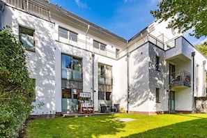 A modern white building with large windows, a balcony, and a well-maintained lawn.