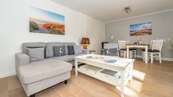 A modern living room with a grey sofa, a white coffee table, and a dining area with white chairs and a table.