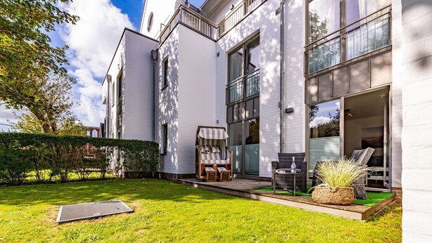 A modern house with a white exterior, a covered patio with outdoor furniture, and a well-maintained lawn. - Stadtresidenz App. 4 - Ebenerdige, Moderne Stadtwohnung- Kurze Wege zum Strand, mit Eigener (Sylt)