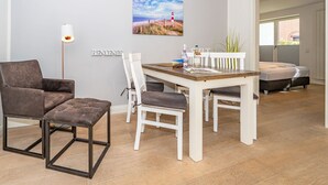 A modern, well-lit room with a wooden dining table, white chairs, a brown leather sofa, and a small bench. A painting of a lighthouse is on the wall, and a lamp is on the floor. - Stadtresidenz App. 4 - Ebenerdige, Moderne Stadtwohnung- Kurze Wege zum Strand, mit Eigener (Sylt)