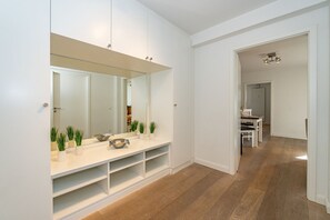 Ein modernes Badezimmer mit einem großen Spiegel, weißen Schränken und einem Waschtisch. Auf dem Waschtisch stehen Blumentöpfe und im Hintergrund ist eine Dusche zu sehen.