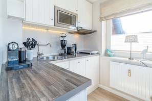 A modern kitchen with white cabinetry, a built-in microwave, a coffee machine, and a window with a view of the outside.