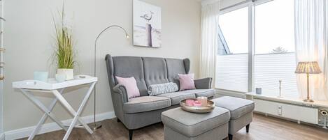 A modern living room with a grey sofa, a small white table, and a potted plant.