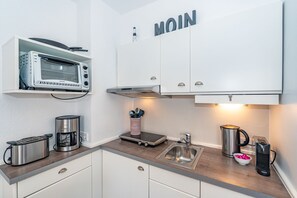 Una cocina moderna con armarios blancos, microondas integrado, hervidor y cafetera.