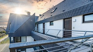 A modern building with a sloped roof, a balcony with metal railings, and a view of the sky.