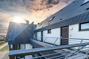 A modern building with a sloped roof, a balcony with metal railings, and a view of the sky. - Möwennest App. 18 - Cozy 2-room vacation apartment with balcony in (Wenningstedt-Braderup (Sylt))