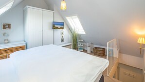 A bedroom with a large bed, a wardrobe, a desk, a television, and a skylight.