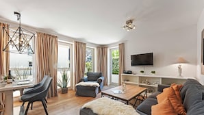 A modern living room with a sofa, a dining area with a table, and a TV mounted on the wall. - Beach Suite, App. 2 - Nah am Meer- Sand im Haar und Salz in der Luft (Sylt)