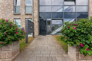 A building entrance with a brick facade, a glass door, and a staircase leading to an upper level. - Beach Suite, App. 2 - Nah am Meer- Sand im Haar und Salz in der Luft (Sylt)