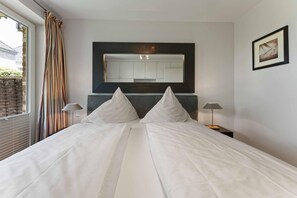 A hotel room with a large bed, two bedside lamps, a headboard, a mirror, and a framed picture on the wall. - Beach Suite, App. 2 - Nah am Meer- Sand im Haar und Salz in der Luft (Sylt)