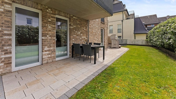 A residential building with a brick exterior, a balcony, a patio with a table and chairs, and a well-maintained lawn. - Beach Suite, App. 2 - Nah am Meer- Sand im Haar und Salz in der Luft (Sylt)