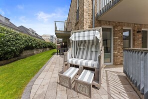 A balcony with a striped lounge chair, a small table, and a wicker basket.