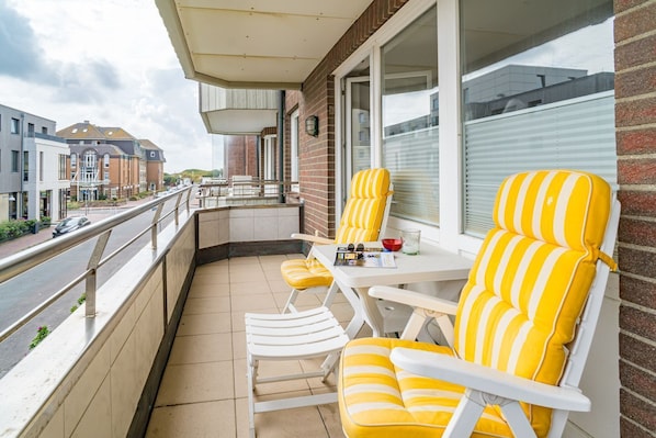Ein Balkon mit gelb gestreiften Stühlen und einem Tisch, mit Blick auf eine Straße mit Gebäuden.
