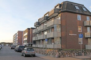 A multi-story residential building with a brick facade, balconies, and a parking sign indicating a parking area.