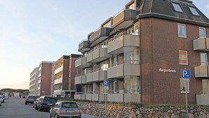 A multi-story residential building with a brick facade, balconies, and a parking sign indicating a parking area. - Margaretheneck App. 5 - 2-room vacation apartment close to the beach for max. 2 people (Sylt)