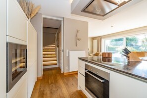A modern kitchen with a built-in oven, a wooden staircase, and a large window offering a view of the outdoors. - Winterhuus - Fantastic vacation home with garden and sauna in the south of (Sylt)