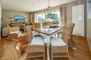 A dining area with a wooden table and wicker chairs, a sofa, and a television in the background. - Winterhuus - Fantastic vacation home with garden and sauna in the south of (Sylt)