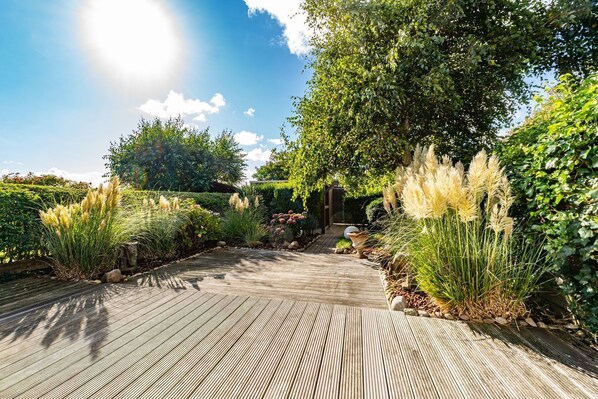 A wooden pathway leading through a garden with various plants and trees. - Winterhuus - Fantastic vacation home with garden and sauna in the south of (Sylt)