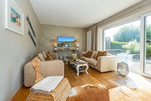 A modern living room with a large TV, comfortable seating, and a view of the outdoors. - Winterhuus - Fantastic vacation home with garden and sauna in the south of (Sylt)