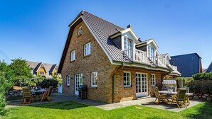 Une maison à deux étages, construite en briques, avec un toit en pente, un balcon et une pelouse bien entretenue.