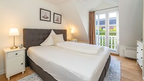 Une chambre avec un grand lit, deux tables de chevet avec des lampes, une fenêtre avec des rideaux et deux tableaux encadrés accrochés au mur.