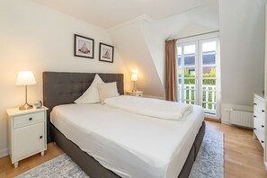 Un dormitorio con una cama grande, dos mesitas de noche con lámparas, una ventana con cortinas y dos cuadros en la pared.