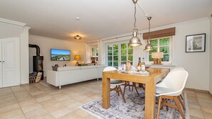 Un salon spacieux comprenant un canapé, une table à manger avec des chaises, une cheminée et une grande fenêtre donnant sur un paysage verdoyant.