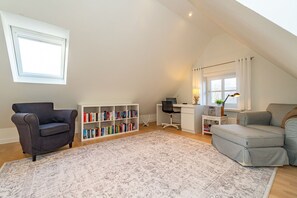 A spacious loft with a high ceiling, a large window, a built-in bookshelf, a desk, a comfortable armchair, and a grey sofa.