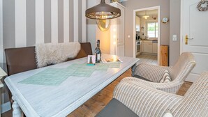 A dining area with a table, chairs, a hanging light fixture, and a view into the kitchen. - Constantin - 3-room vacation apartment for up to 4 people with garden and (Sylt)