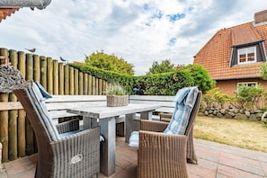 Eine Terrasse im Freien mit einem Holztisch und Korbstühlen, umgeben von einem Holzzaun und Grünpflanzen.