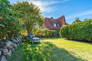 A house with a sloped roof, a stone wall, and a well-maintained lawn.