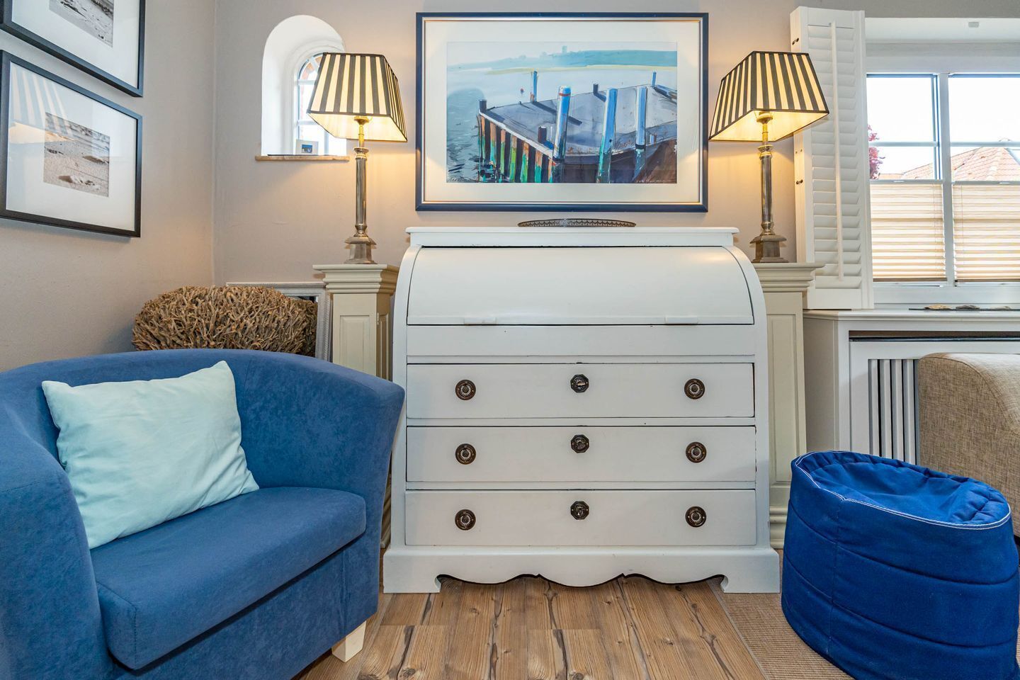 A living room with a blue sofa, a white chest of drawers, a blue bean bag, and two lamps.