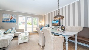 A cozy living room with a sofa, a coffee table, and a dining table. There is a painting on the wall and a television on the table. - Constantin - 3-room vacation apartment for up to 4 people with garden and (Sylt)