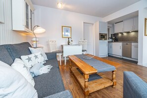 Un salon moderne comprenant un canapé, un banc en bois, une table à manger et un coin cuisine avec des placards et des appareils électroménagers.