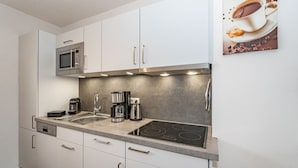 Een moderne keuken met witte kastjes, een roestvrijstalen magnetron, een koffiezetapparaat en een kookplaat.
