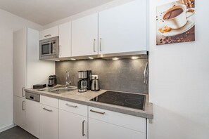 A modern kitchen with white cabinets, a stainless steel microwave, a coffee maker, and a stovetop.