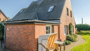 Een klein huis van baksteen met een schuin dak, een raam en een terras met een stoel en tafel.