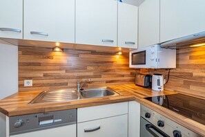 A compact kitchen with a wooden backsplash, stainless steel sink, microwave, toaster, and dishwasher.