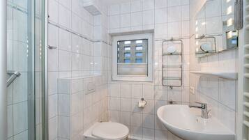Ein kleines Badezimmer mit Duschkabine aus Glas, Toilette, Waschbecken und Fenster.