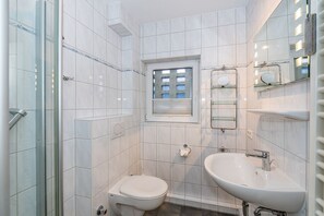 Uma casa de banho compacta com cabine de duche em vidro, sanita, lavatório e janela.