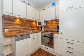 Une cuisine compacte avec des meubles blancs, un plan de travail en bois, un four à micro-ondes encastré, une machine à café et un lave-vaisselle.