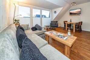 A modern living room with a sofa, a dining table, and a TV mounted on the wall.