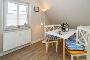 Un área de comedor con una mesa blanca, sillas de estampado azul y blanco, una lámpara de pie y un ventanal con persianas.
