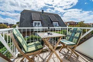 Un balcon avec deux chaises à motifs écossais, une petite table en bois et une bouteille de vin.