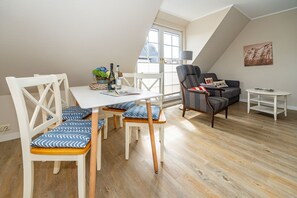 Ein modernes Wohnzimmer mit Essbereich, ausgestattet mit einem weißen Tisch, blau-weißen Stühlen, einem grauen Sofa und einem kleinen weißen Beistelltisch.