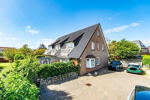 Ein zweistöckiges Haus mit geneigtem Dach, einer Steinmauer und einem gepflasterten Einfahrtsweg.