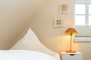 Ein Schlafzimmer mit einem Bett, einem Nachttisch, einer Lampe und zwei gerahmten Bildern an der Wand.