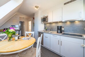 A modern kitchen with white cabinets, a microwave, a coffee maker, and a dining area with a table and chairs. - Strandberg II - 3-room apartment for up to 4 people - only 400 meters to the beach (Sylt)